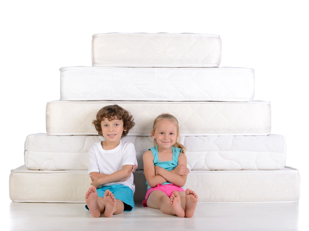 Young children sitting on lots of mattresses isolated on white background
