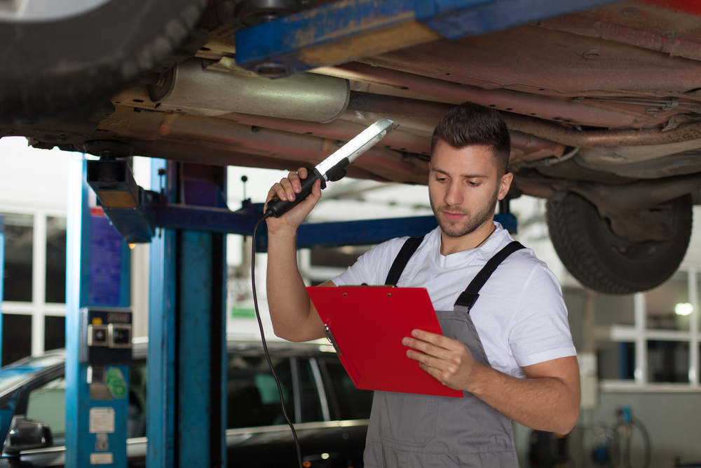 Auto,Mechanic,Check,List.,Focused,Mechanic,Standing,Under,The,Car